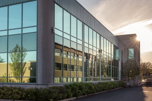 Exterior of a modern commercial building with large windows and wall-mounted lighting at sunset.